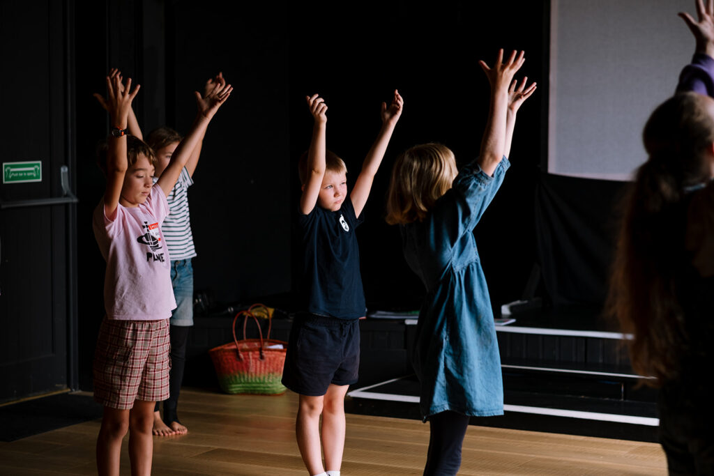 Image of children holding their hands up in front of a stage