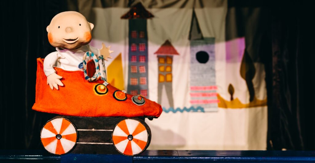 Image of a puppet baby in a red shoe which is on wheels