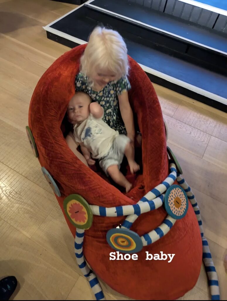 Girl and baby sitting in a giant red shoe