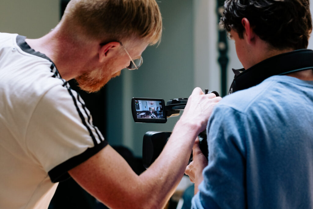 Image of a young person and an adult looking into a film camera